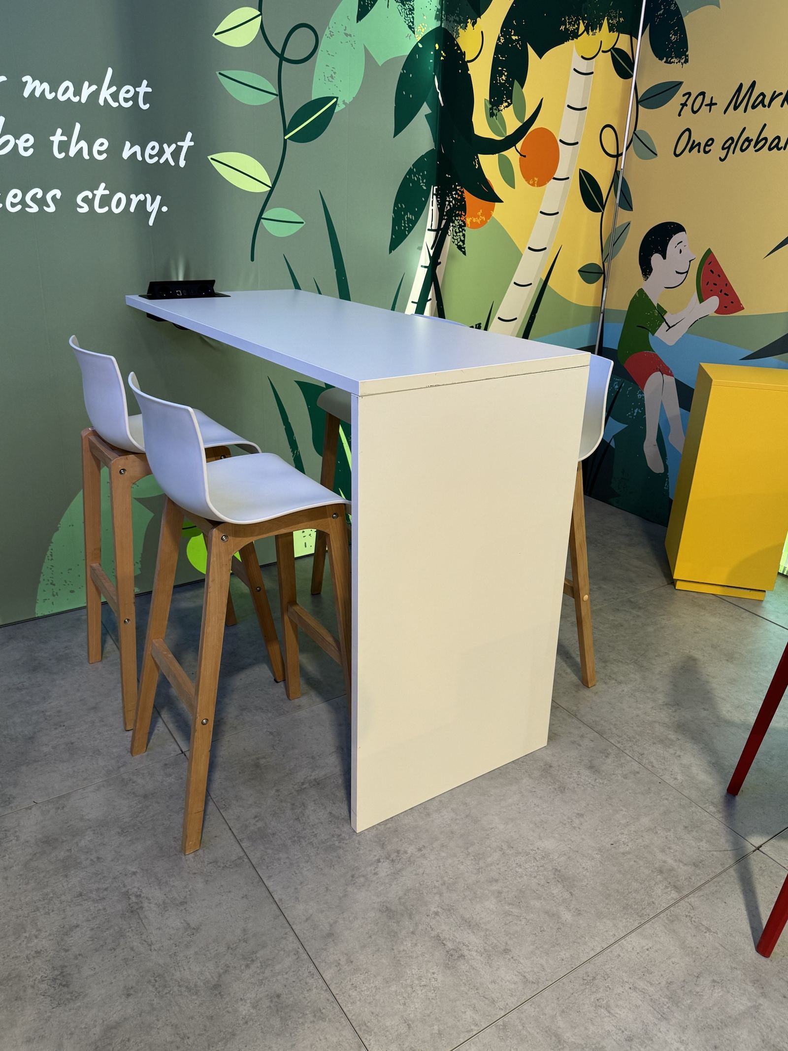 Stehtisch mit wei&szlig;en Barhockern vor der Illustrationswand